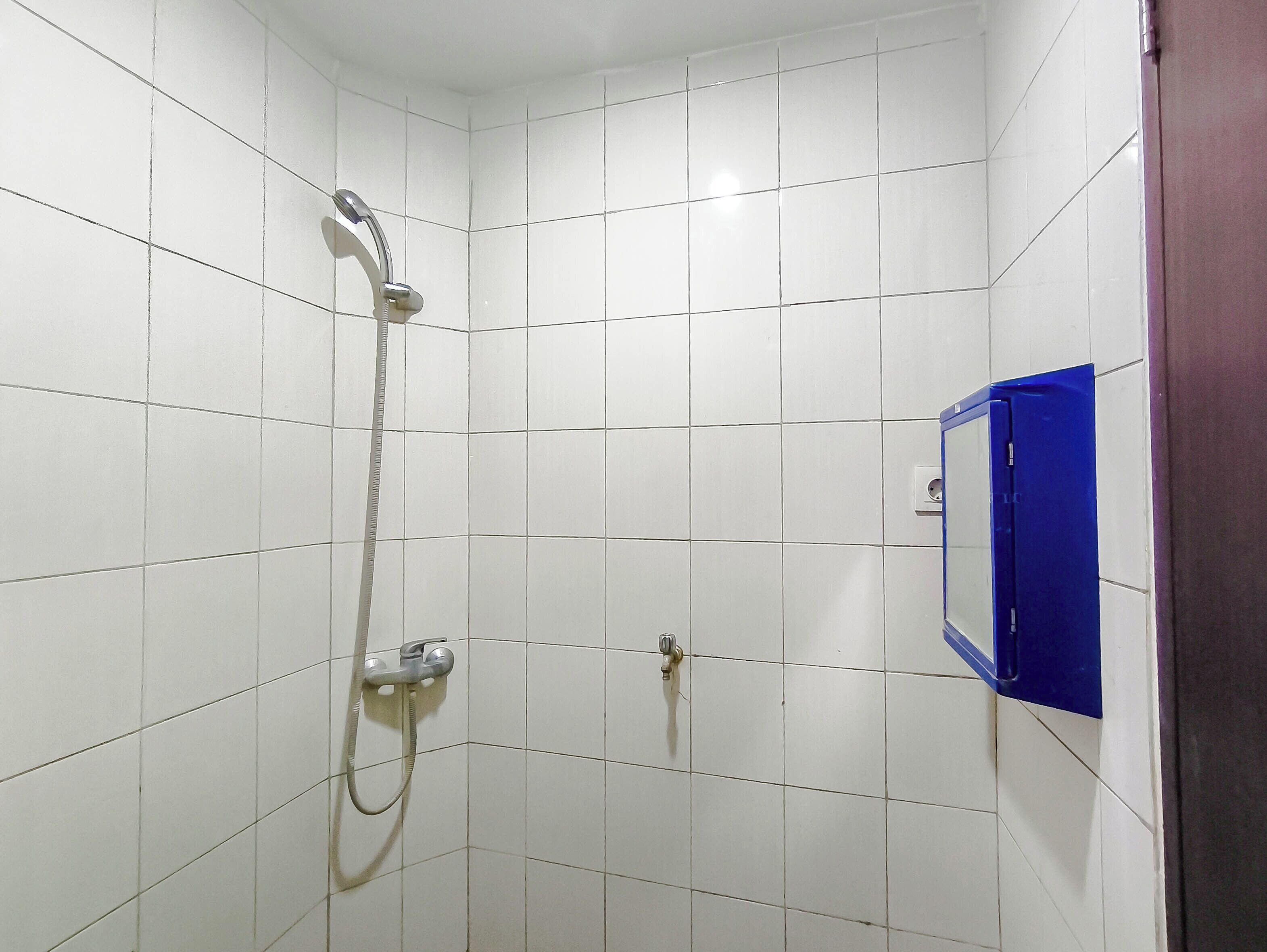 A bathroom with white tiled walls, a shower with a handheld showerhead, and a blue medicine cabinet.