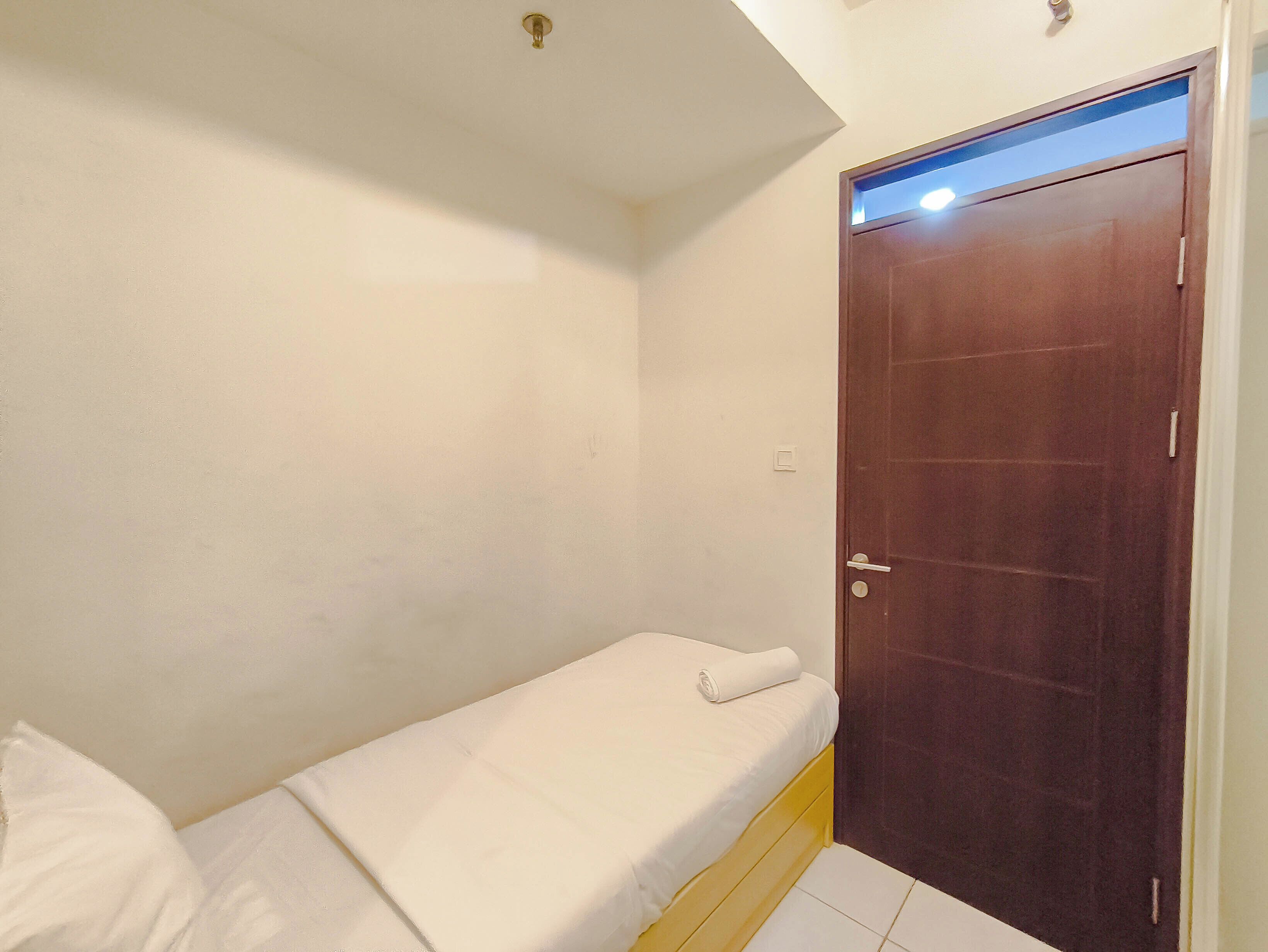 Quarto pequeno com uma cama de solteiro, porta de madeira e paredes brancas.