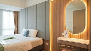 A modern hotel room with a bed, a large mirror, a vanity with a sink, and a small stool. - Calm Tone 1Br At Tokyo Riverside Pik 2 Apartment (Teluknaga)