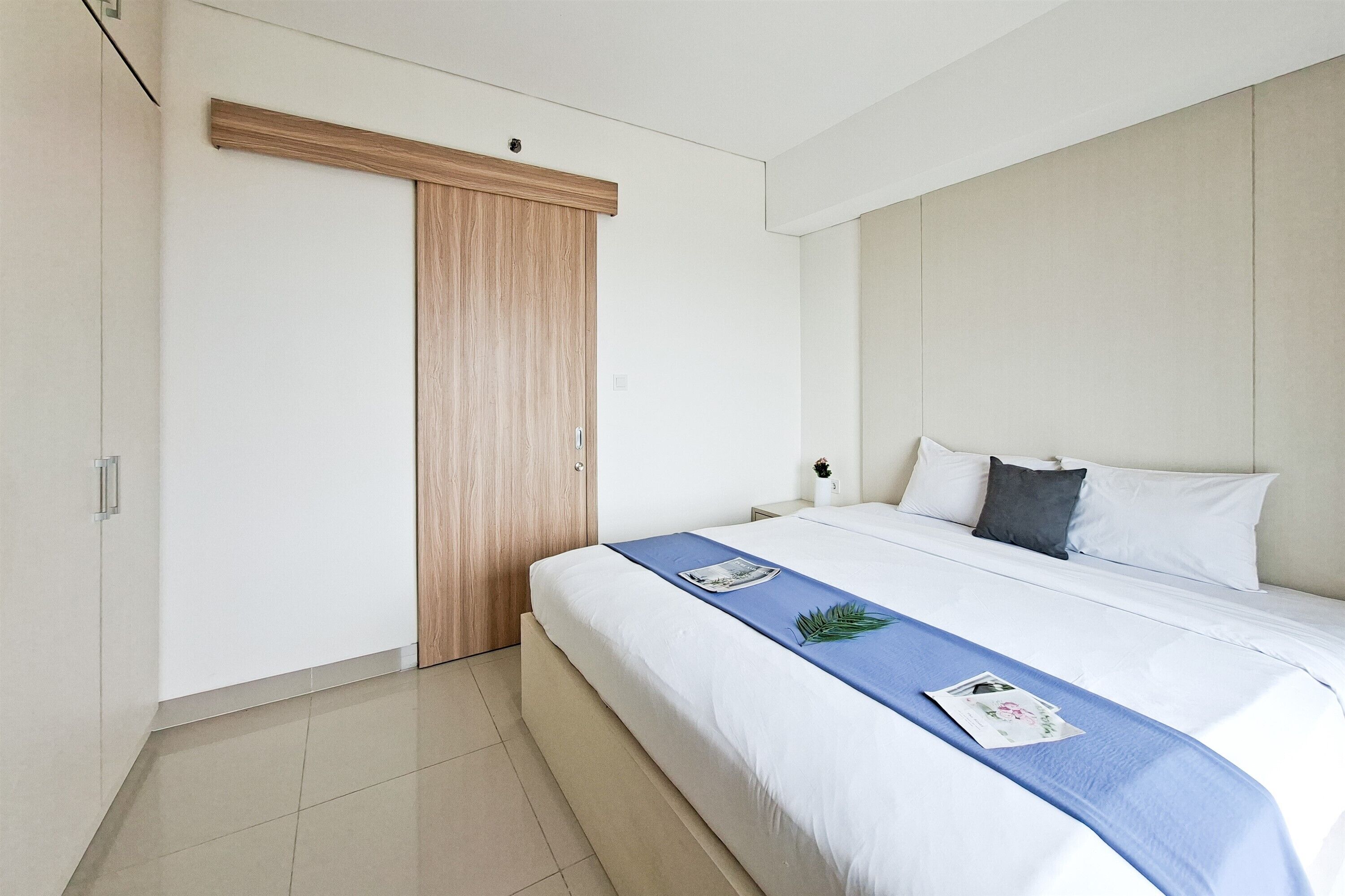 A modern bedroom with a large bed, a wooden wardrobe, and a white headboard.