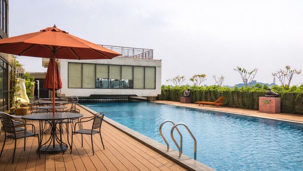 A rooftop pool area with a wooden deck, outdoor seating, and a modern building with large windows. - Simple Stay Studio Near Ui At Dave Apartment (Depok)