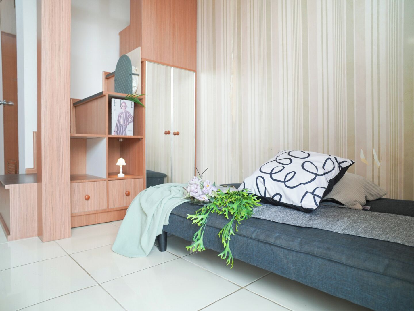 A modern bedroom with a grey sofa, a wooden wardrobe, and a bed with a patterned pillow.