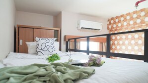 A bedroom with a bunk bed, a single bed with a green blanket, a white pillow with a black pattern, and a small plant on the bed. - Simple Stay Studio Near Ui At Dave Apartment (Depok)