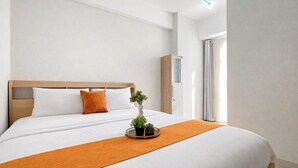 Una cama bien hecha con ropa blanca, un edredón naranja y una planta pequeña sobre una bandeja.