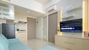 Una sala moderna con un sofá azul claro, un televisor de pantalla plana montado en una pared de mármol y una zona de cocina con un refrigerador y armarios.