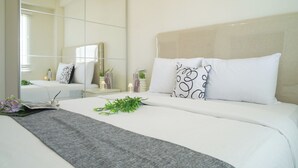 A neatly arranged bedroom with a large mirror, a bed with white bedding, and a grey throw blanket. - Contemporary And Comfortable 2Br At Apartment Podomoro Golf View (Gunung Putri)