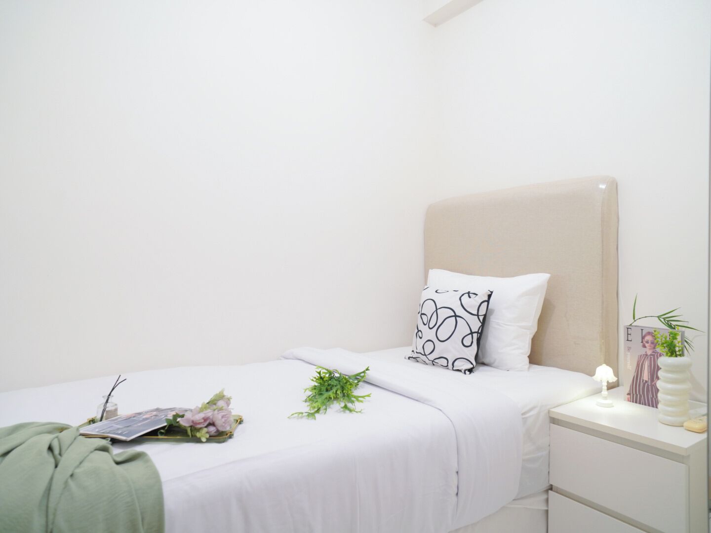 Un dormitorio minimalista con una cama individual, una mesita de noche con lámpara y una pequeña planta en maceta.