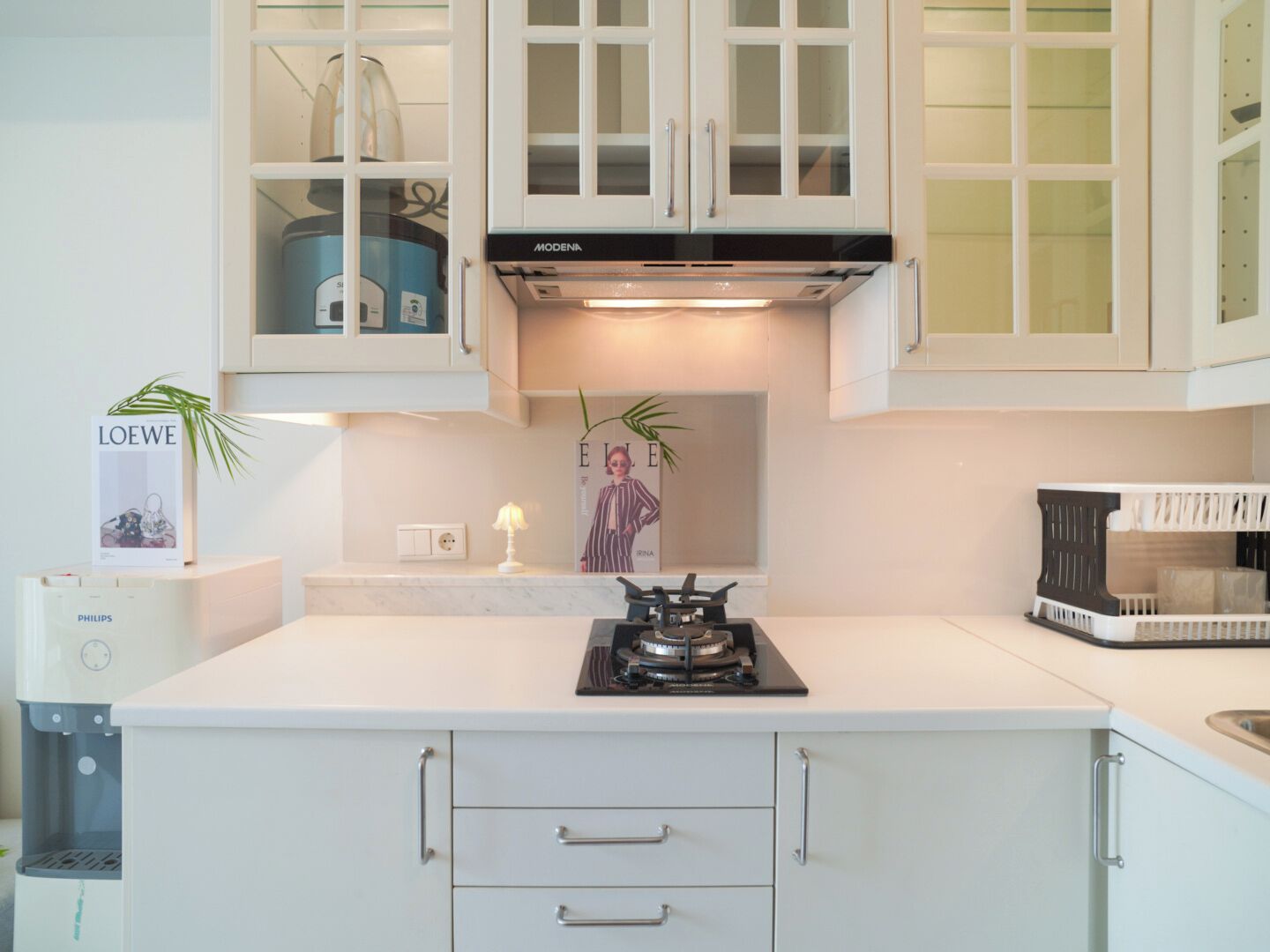 Een moderne keuken met witte kastjes, een gasfornuis en een inbouwoven. Op het aanrecht staan decoratieve items en een tijdschrift.