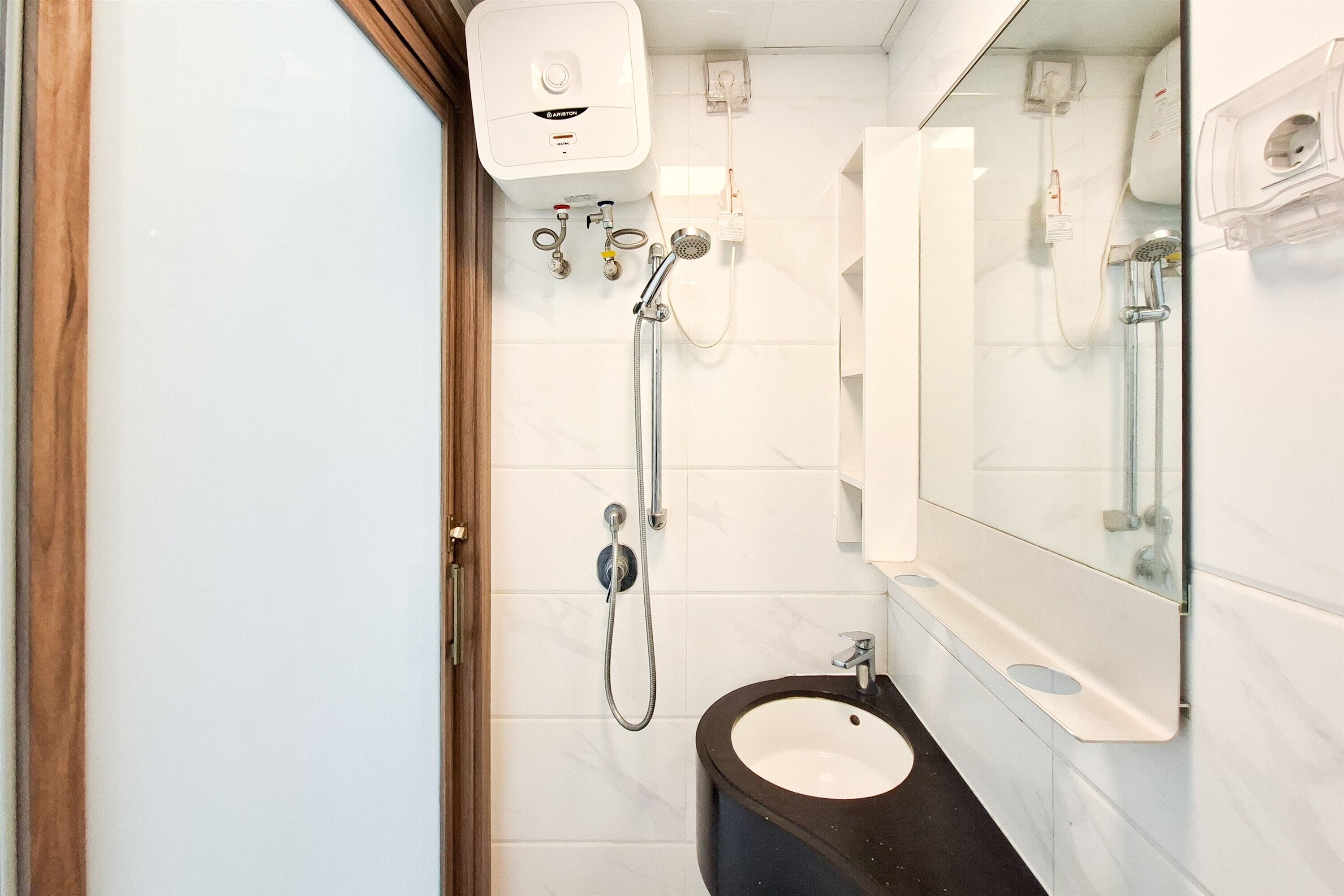 Un baño con pared de azulejos blancos, un lavabo negro, un espejo y una ducha con cabezal de mano.