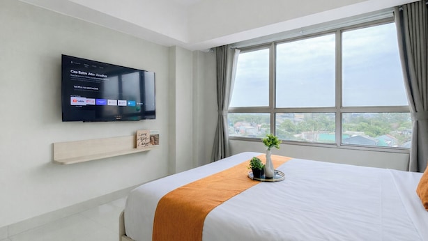 Ein Hotelzimmer mit einem Bett, einem an der Wand montierten Fernseher, einem Fenster mit Aussicht und einem Regal mit einer kleinen Pflanze und einem Schild.