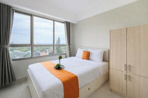 Ein Hotelzimmer mit großem Fenster, einem Bett mit weißer Bettwäsche und einer orangefarbenen Decke, einem Holzschrank und einer kleinen Pflanze auf dem Bett.