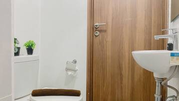 Ein Badezimmer mit Toilette, einer Holztür, einem Waschbecken und zwei Blumentöpfen.