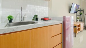 A modern kitchen with a marble countertop, wooden cabinets, a stainless steel sink, and a built-in red induction cooktop. - Modern Studio Apartment Near Sicc At Royal Sentul Park (Bogor)