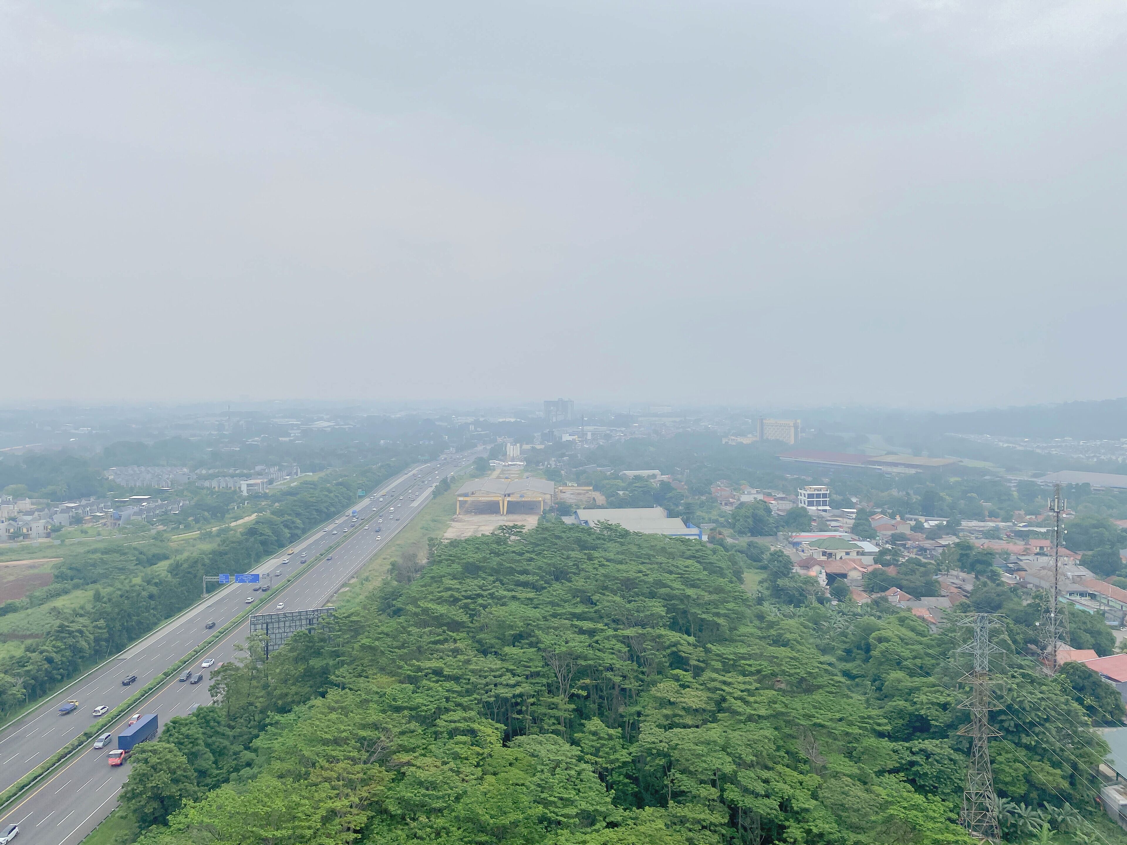 Une vue aérienne d’une ville avec une autoroute, une végétation luxuriante et divers bâtiments.