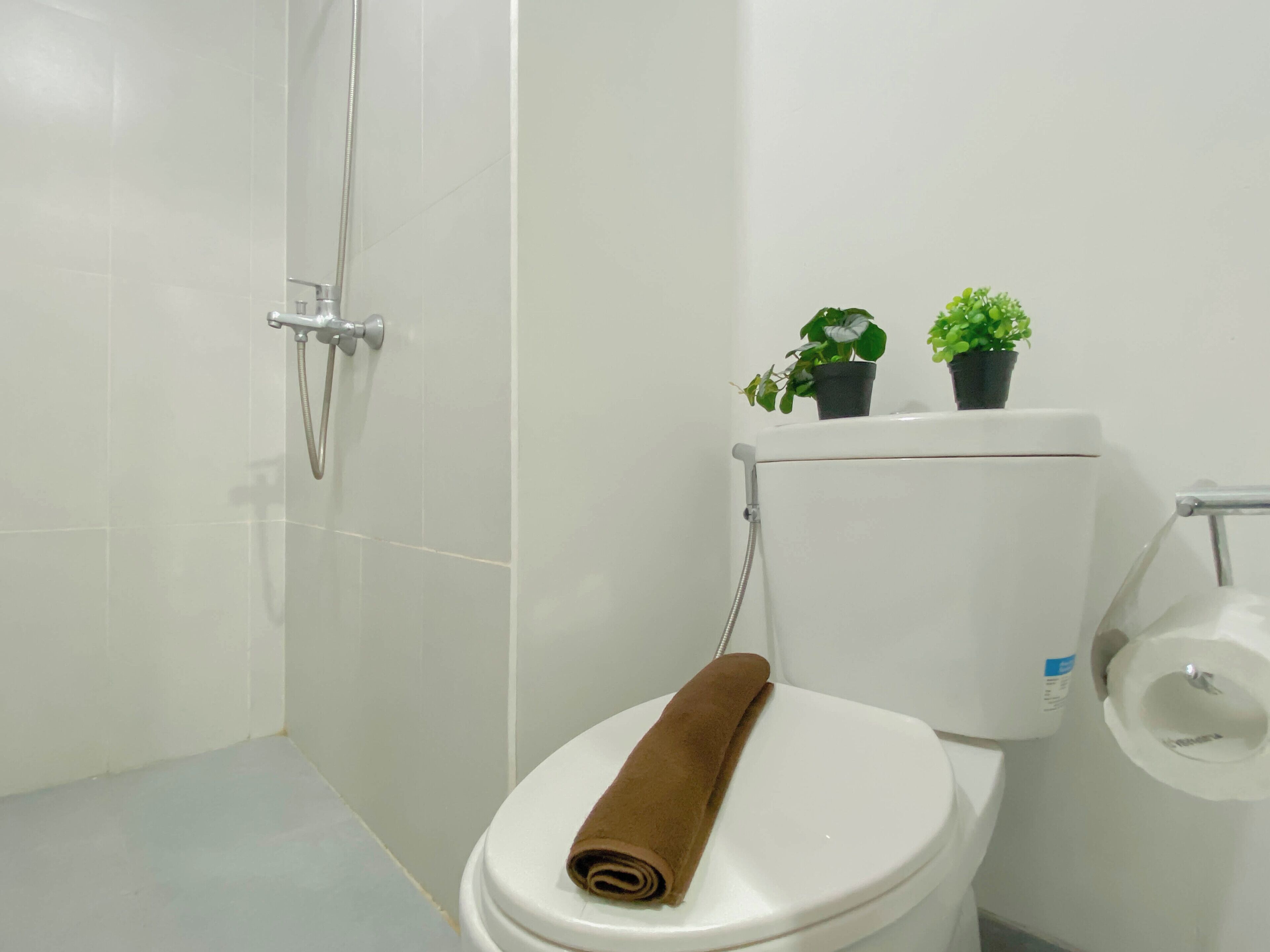A bathroom with a white toilet, a shower, and two potted plants on the toilet tank.