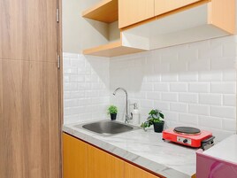 Una cocina con protector contra salpicaduras de azulejos blancos, armarios de madera, un lavamanos de acero inoxidable, una estufa portátil roja y dos plantas en macetas.