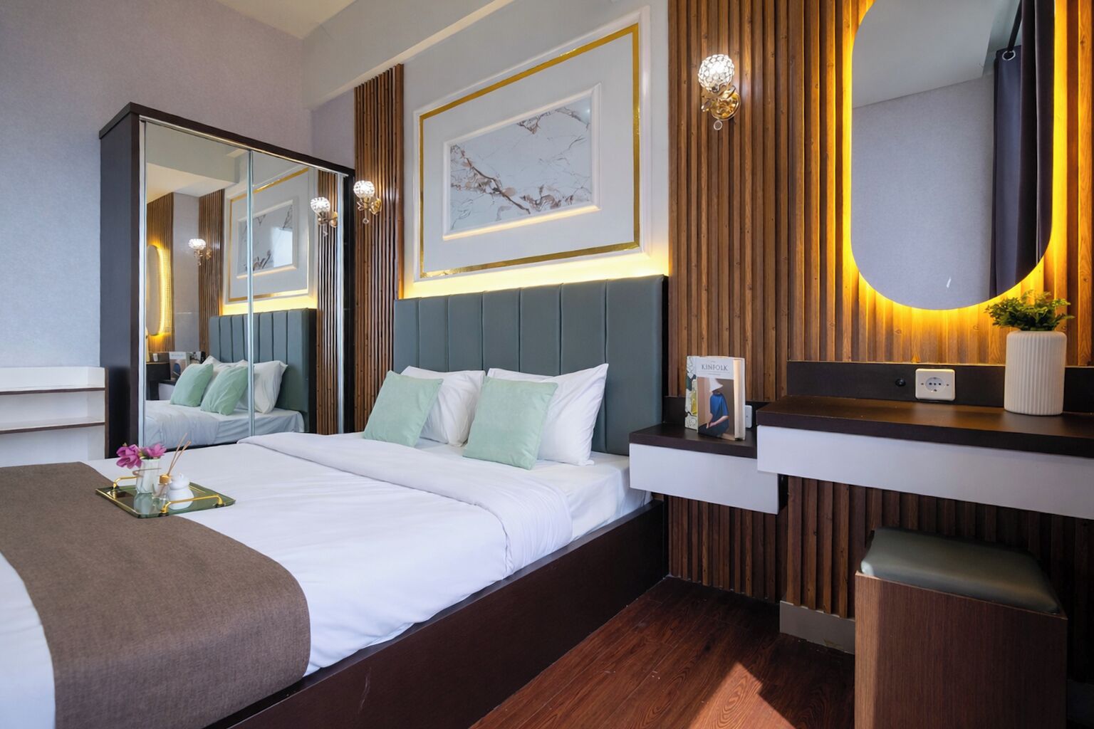 Una habitación de hotel moderna con una cama grande, una mesita de noche con lámpara, un espejo y una obra de arte enmarcada en la pared.