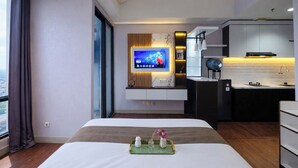 Een moderne hotelkamer met een groot bed, een aan de muur bevestigde televisie, een kleine kitchenette en uitzicht door een raam.