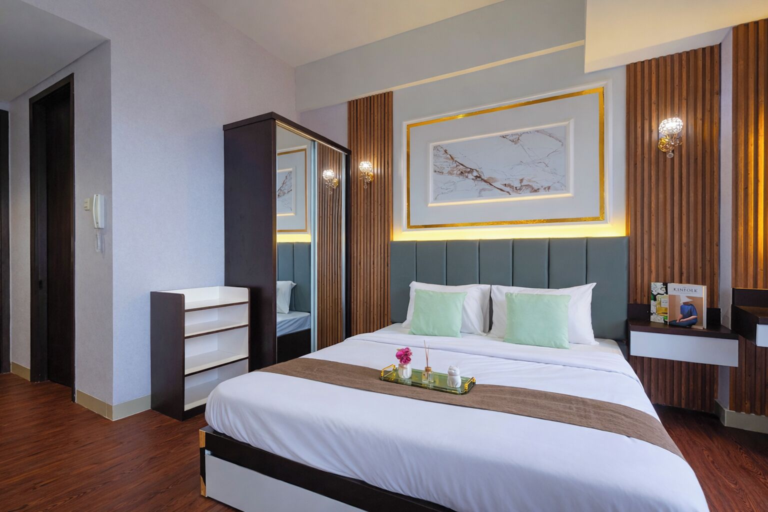 A modern hotel room with a large bed, a bedside table, a mirror, and a wall-mounted artwork.