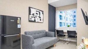 A modern kitchen with a grey sofa, a black refrigerator, and a dining area with two chairs. - Tranquil 1Br At Royal Sentul Park Apartment (Bogor)
