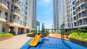 Een speelplaats met een glijbaan en schommels, omringd door appartementencomplexen.