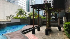 A swimming pool with a wooden deck, a pergola with plants, and a staircase leading to a building. - Tranquil Studio At Tamansari Semanggi Apartment (Jakarta)