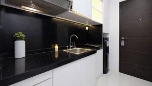 A modern kitchen with a black countertop, stainless steel sink, and a built-in range hood. - Tranquil Studio At Tamansari Semanggi Apartment (Jakarta)