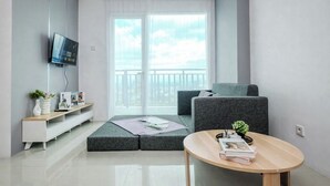 A modern living room with a grey sofa, a small round wooden table, and a TV mounted on the wall. - 2Br Apartment With Service Room And Sofa Bed At Woodland Park Residence (Jakarta)