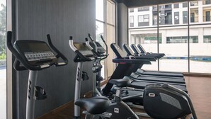 A gym with treadmills and elliptical machines, large windows, and a view of a building outside. - Chic Studio Near Trans Studio Cibubur At Transpark Cibubur Apartment (Depok)