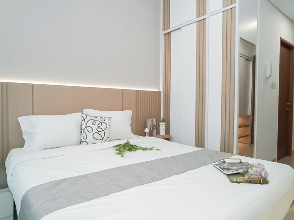 Una habitación de hotel moderna con una cama bien hecha, una mesita de noche con un florero y vista al pasillo.
