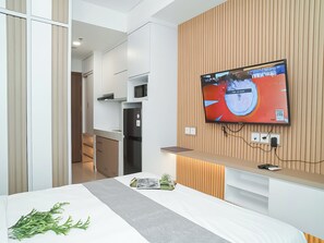 Een moderne hotelkamer met een bed, een aan de muur bevestigde televisie, een magnetron en een kleine kitchenette.