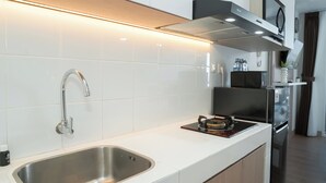 A modern kitchen with white tiles, stainless steel sink, and black appliances. - Tranquil Studio For 2 Pax At Tokyo Riverside Pik 2 Apartment (Teluknaga)