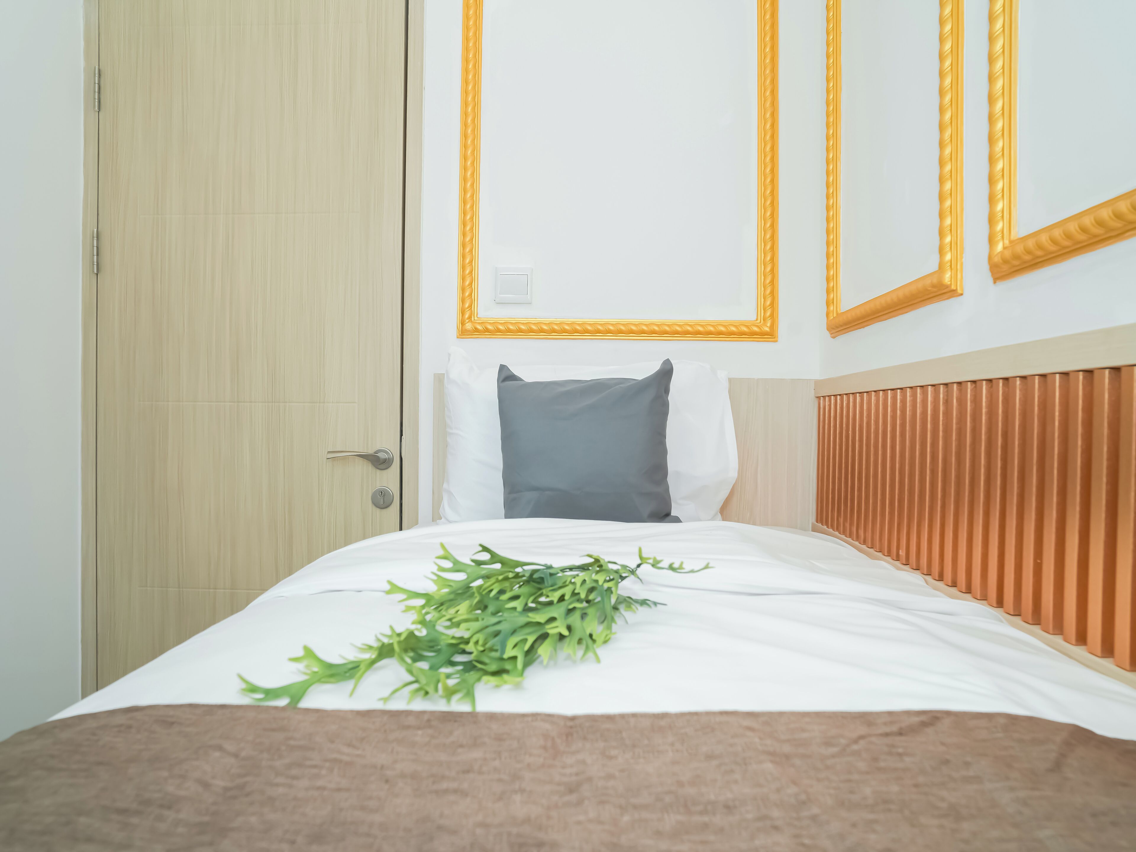 Habitación de hotel con puerta de madera, cama con ropa blanca, almohada gris y manta marrón.