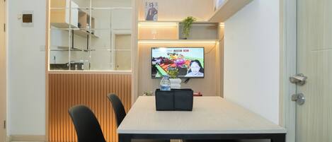 A modern dining area with a wooden partition, a TV displaying a game, and a small plant on a shelf.