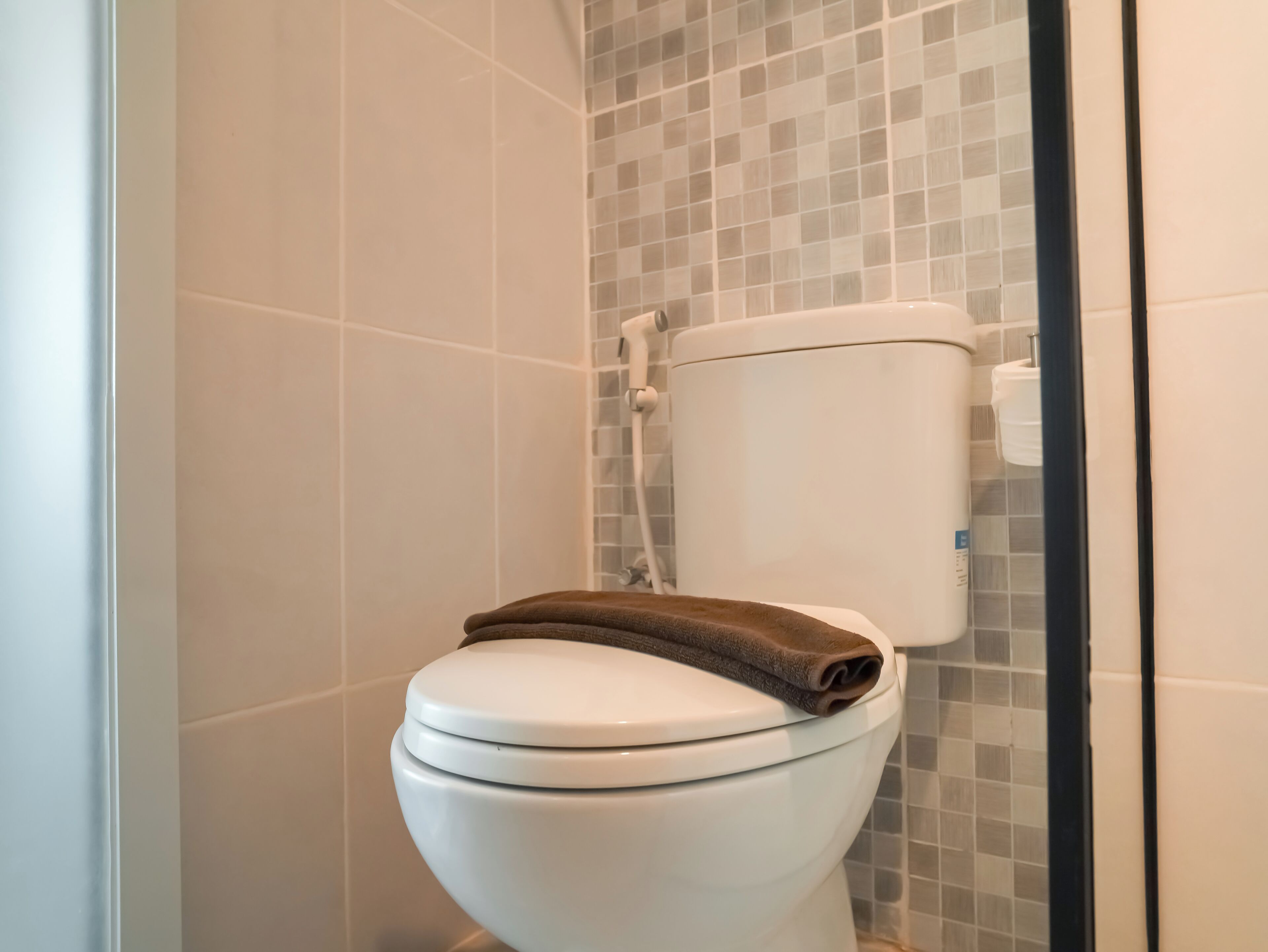 A toilet with a brown towel on top, a tiled wall, and a visible toilet paper holder.