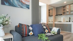 A modern living room with a grey sofa, decorative pillows, a vase with flowers, and a view into the kitchen area. - Contemporary And Enjoyable 1Br At Apartment Tokyo Riverside Pik 2 (Teluknaga)