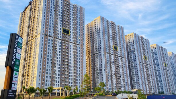 Um edifício residencial alto com várias varandas, uma placa chamativa de hotel e um céu claro.