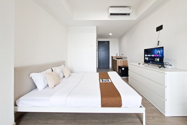 A modern hotel room with a bed, a desk, a television, and an air conditioning unit. - Homelike And Relaxing Studio Apartment Collins Boulevard (Tangerang)