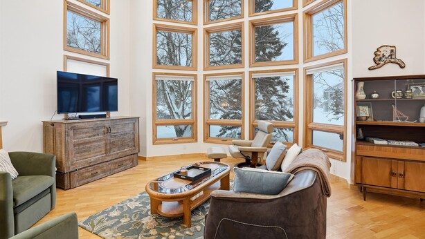A spacious living room with a large window, a television on a wooden cabinet, a sofa, a coffee table, and a fireplace. - 2BR 2BA Quiet Coastal Trail Retreat Near Downtown & Medical Centers (Anchorage)