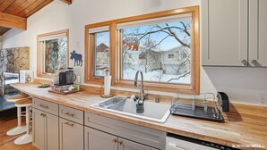 A kitchen with a large window, wooden ceiling, and a stone backsplash. - 2BR 2BA Quiet Coastal Trail Retreat Near Downtown & Medical Centers (Anchorage)