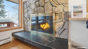 A stone fireplace with a glass door, a window with a view of trees, and a welcome sign on the wall.
