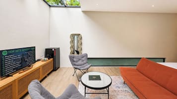A modern living room with a television displaying a Spotify Top Hits list, a grey chair, a round coffee table, and a sofa.
