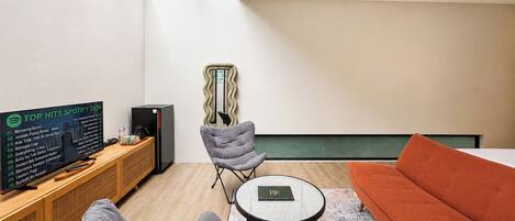 Una sala de estar moderna con un televisor mostrando una lista de éxitos de Spotify, una silla gris, una mesa de centro redonda y un sofá.
