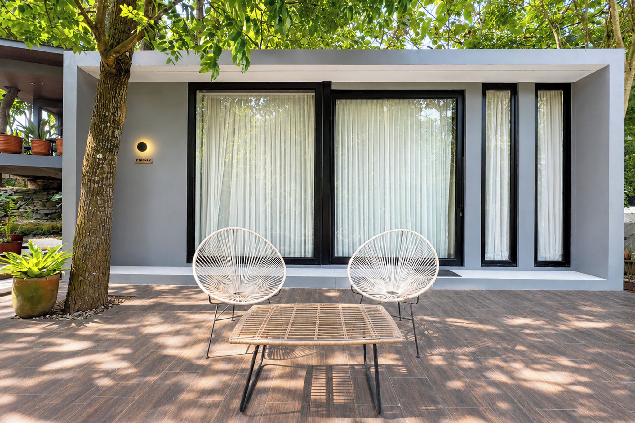 A modern outdoor seating area with a table and two chairs, a tree, and a building with large windows and a sign.