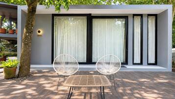 A modern outdoor seating area with a table and two chairs, a tree, and a building with large windows and a sign.