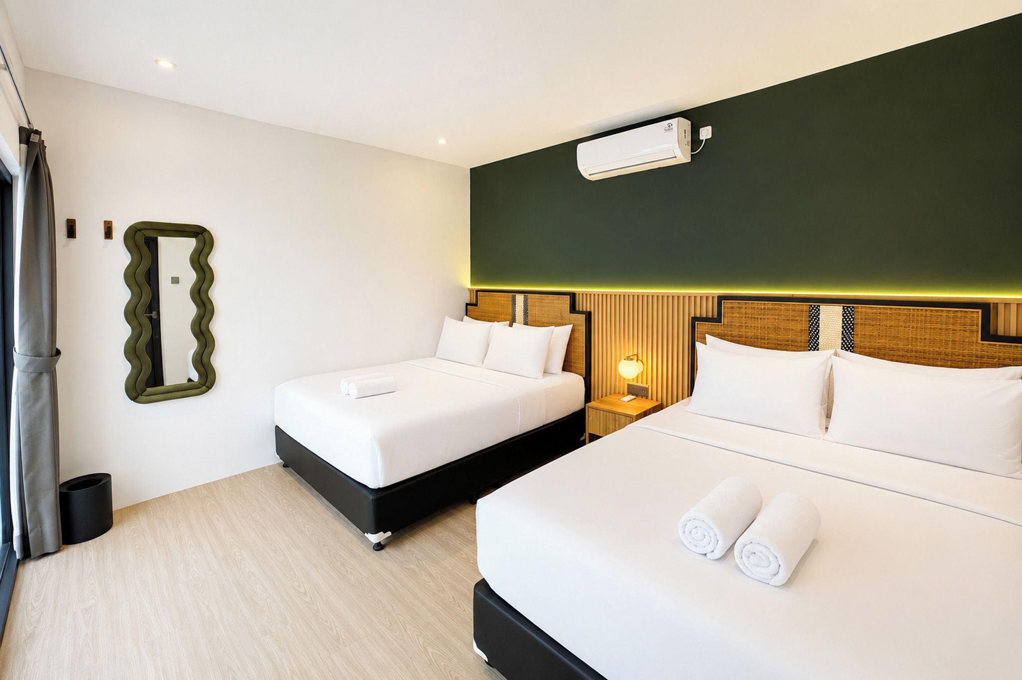 A hotel room with two beds, a mirror, an air conditioning unit, and a bedside lamp.