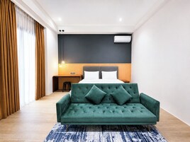 Una habitación de hotel moderna con un sofá verde, un escritorio de madera y una cama con cabecero oscuro.