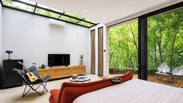 A modern bedroom with a large bed, a TV, a guitar, and a view of a lush forest.