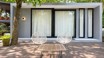 A modern outdoor seating area with a table and two chairs, a tree, and a building with large windows and a sign.
