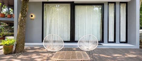 A modern outdoor seating area with a table and two chairs, a tree, and a building with large windows and a sign.